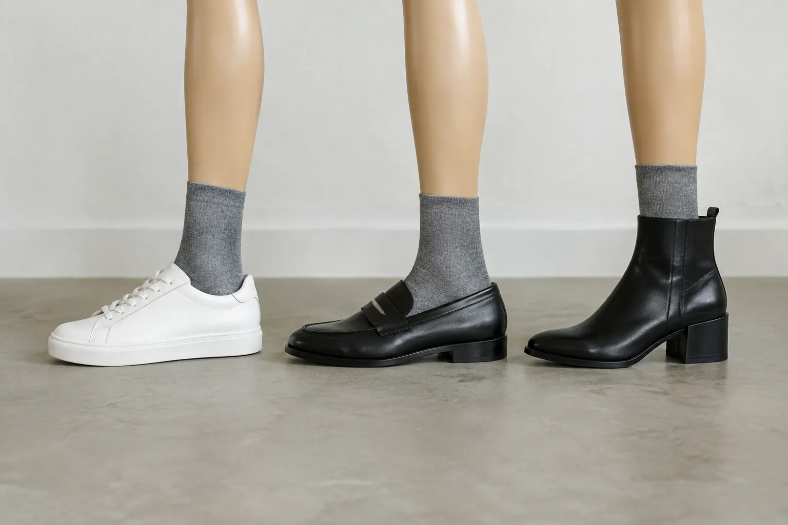Drie paspoponderbenen met grijze sokken in een witte sneaker, zwarte loafer en zwarte enkellaars