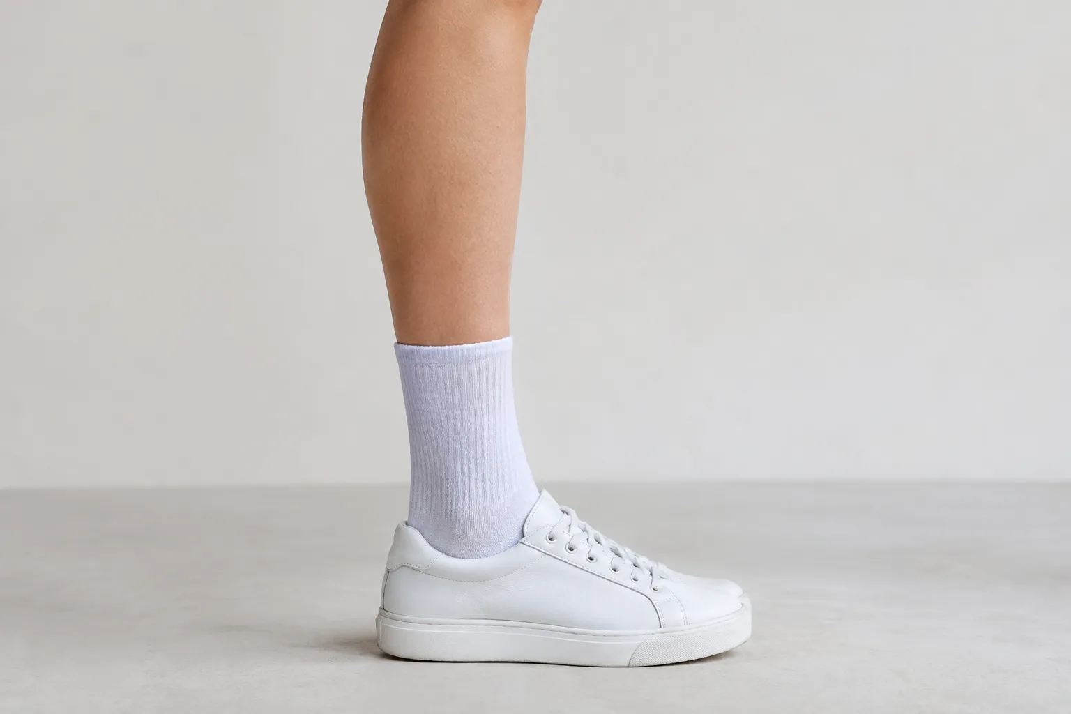 Een onderbeen met een witte crew sok tot onder de kuit en een witte lage sneaker op een lichte vloer