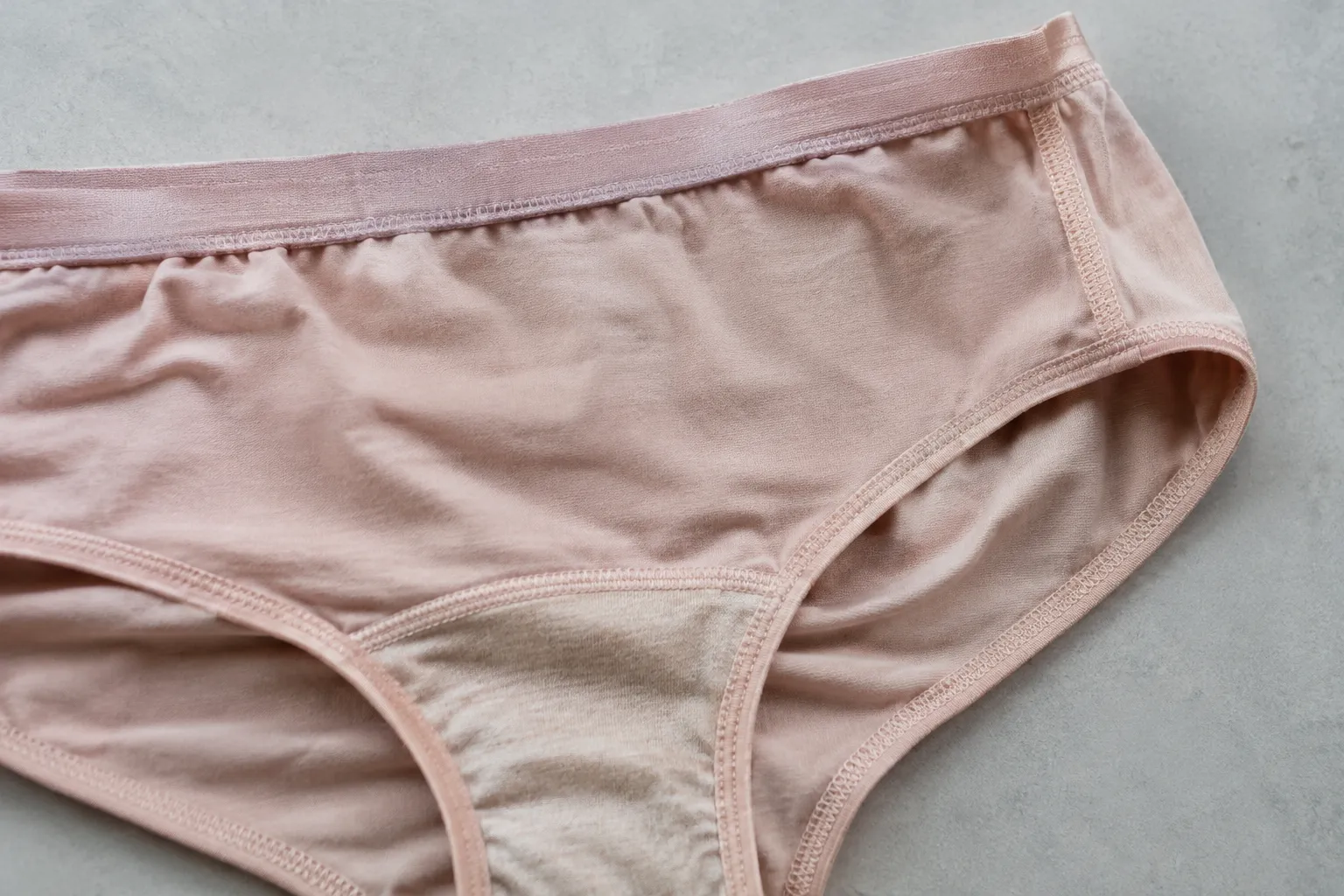 Roze damesslip met zichtbaar kruisje, zijnaad, tailleband en afgewerkte beenopeningen op een grijze ondergrond
