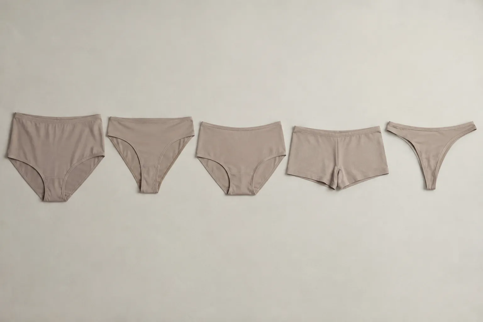 Vijf beige onderbroekmodellen liggen naast elkaar op een effen lichte achtergrond, van tailleslip tot string