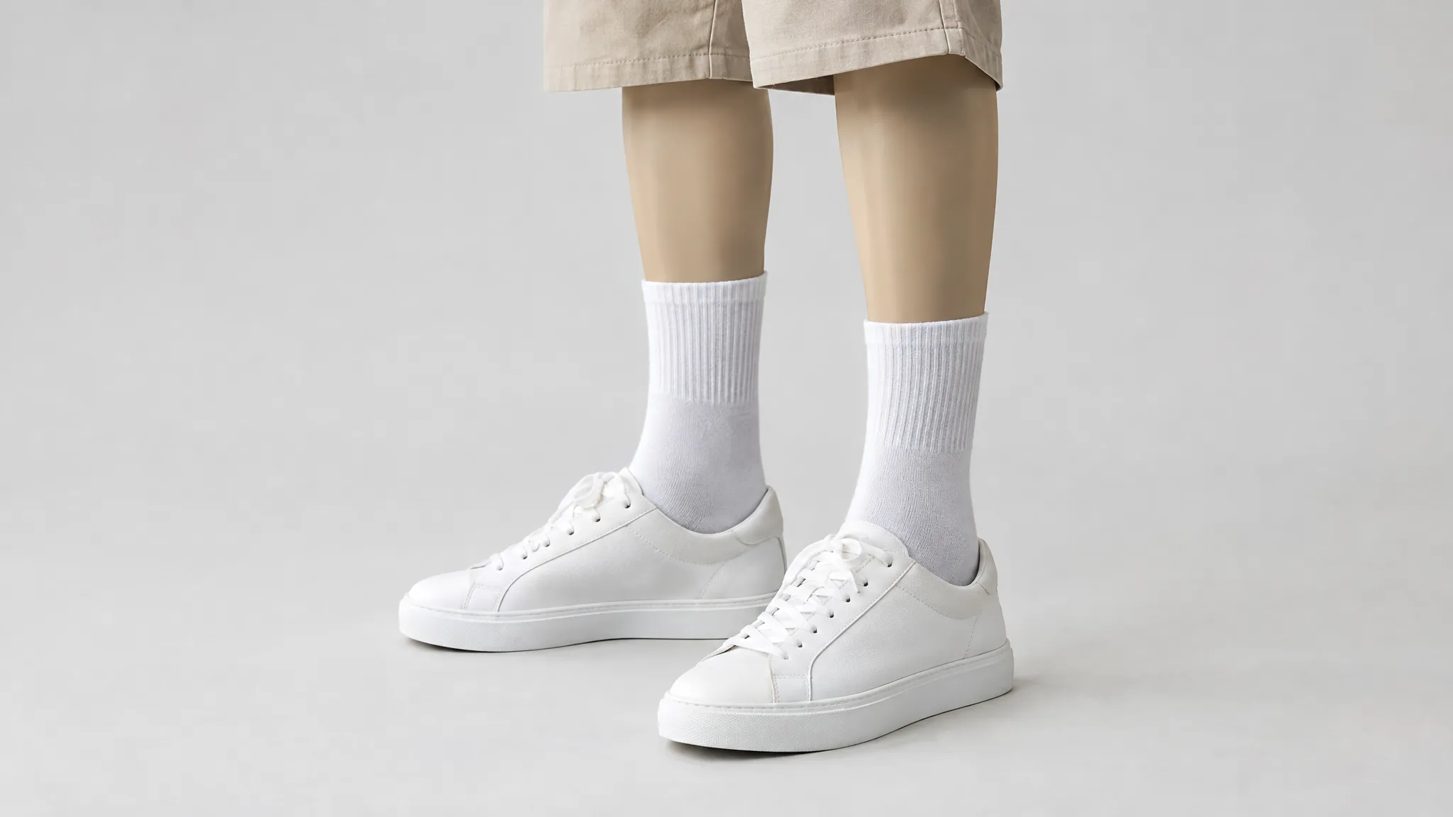 Paspopbenen met witte crew sokken, lage witte sneakers en een beige korte broek tegen een lichte achtergrond