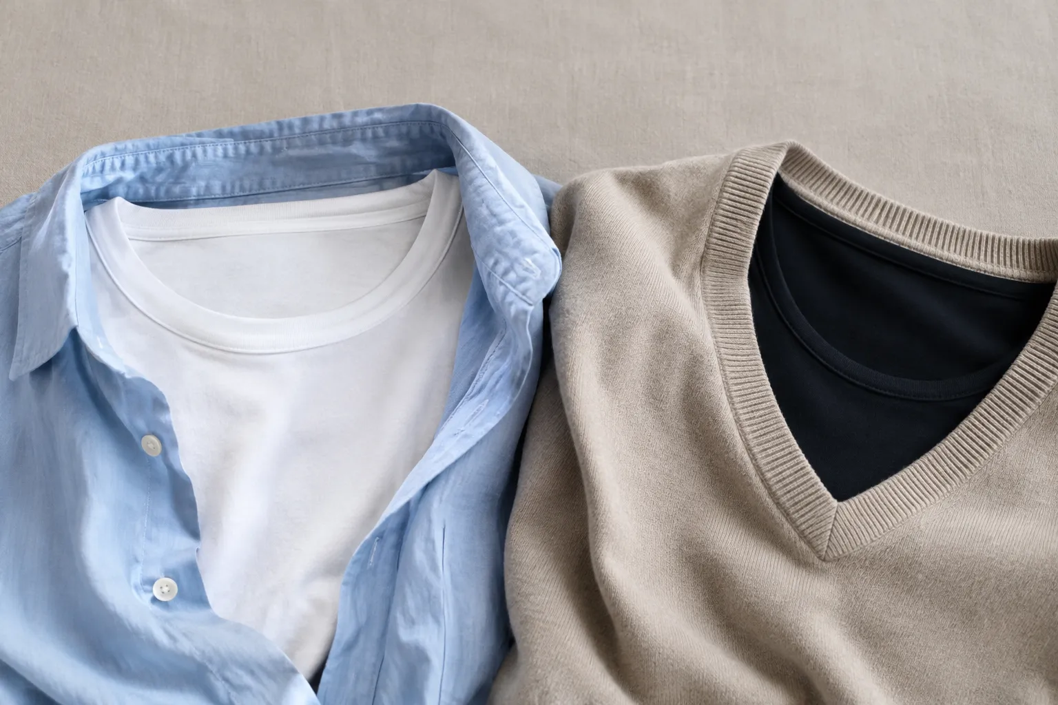 Een wit shirt onder een open lichtblauwe blouse en een zwart shirt met ronde hals onder een beige V-halstrui